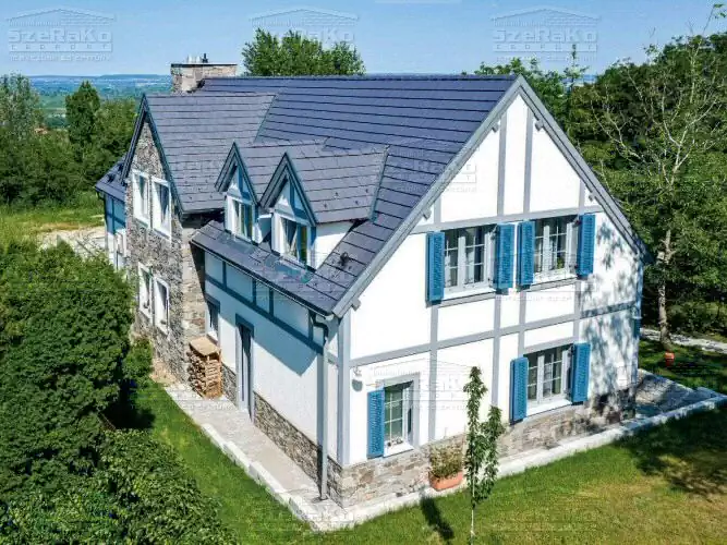 Egyedi fehér tetőteres családi lakóház, szépen gondozott kerttel